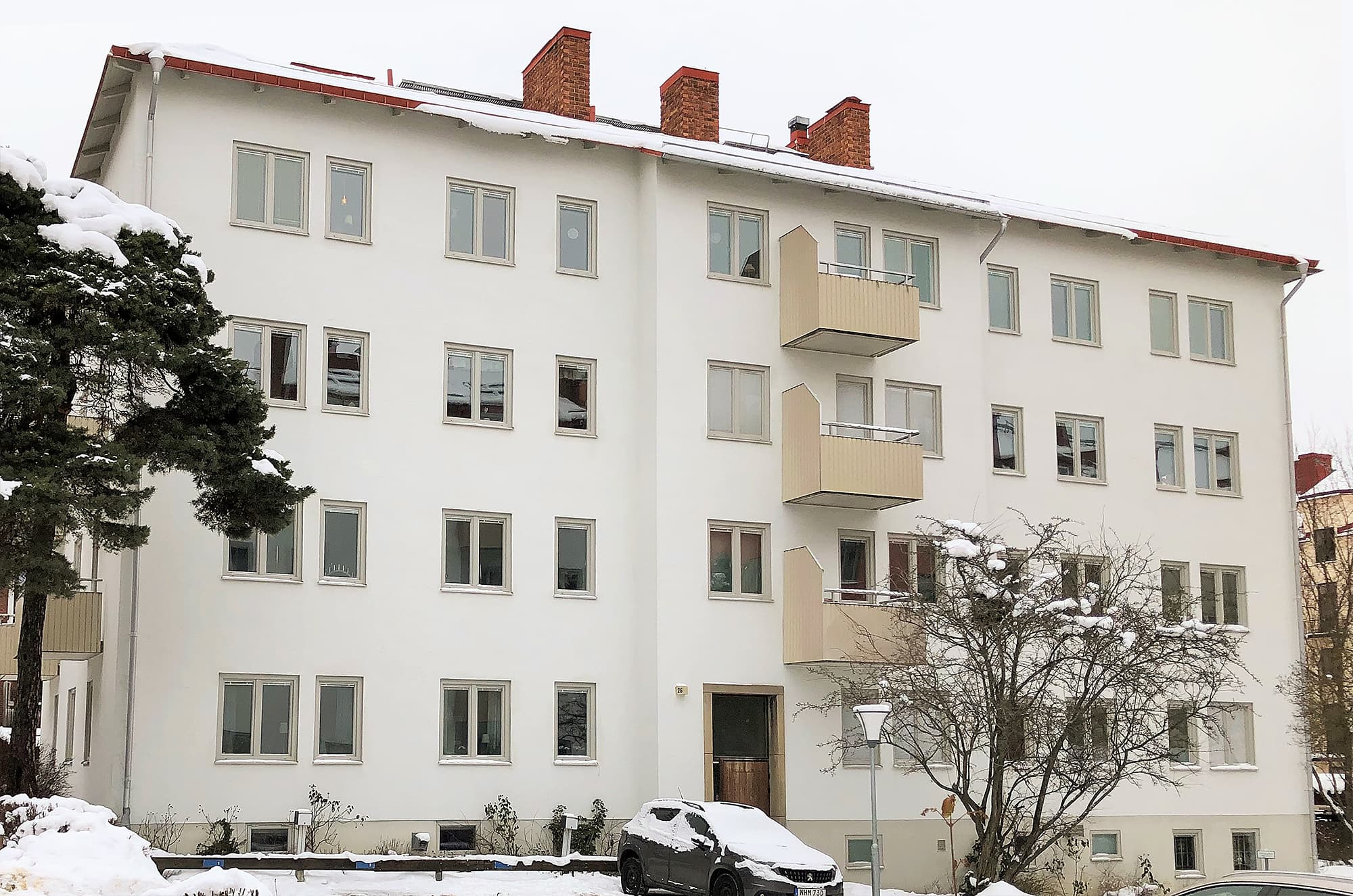 Exteriör av renoverat flervåningshus med nybytta fönster, beige balkonger och vit putsfasad – byte av 210 fönster och Velux takfönster av Mockfjärds.