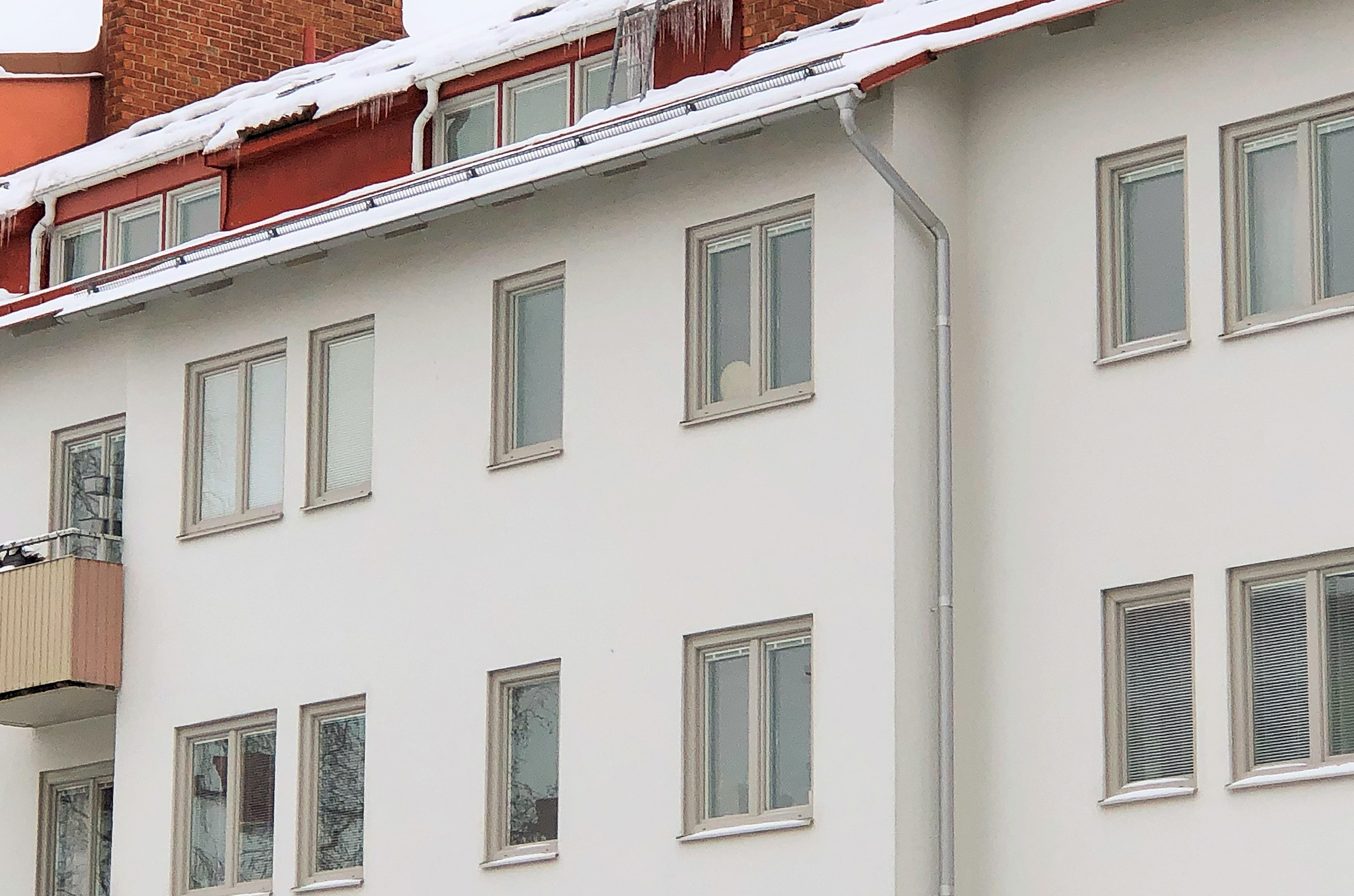 Fasaddetalj med nybytta fönster på vitt flervåningshus – fönsterbyte och takplåtsomläggning runt Velux takfönster utfört av Mockfjärds.