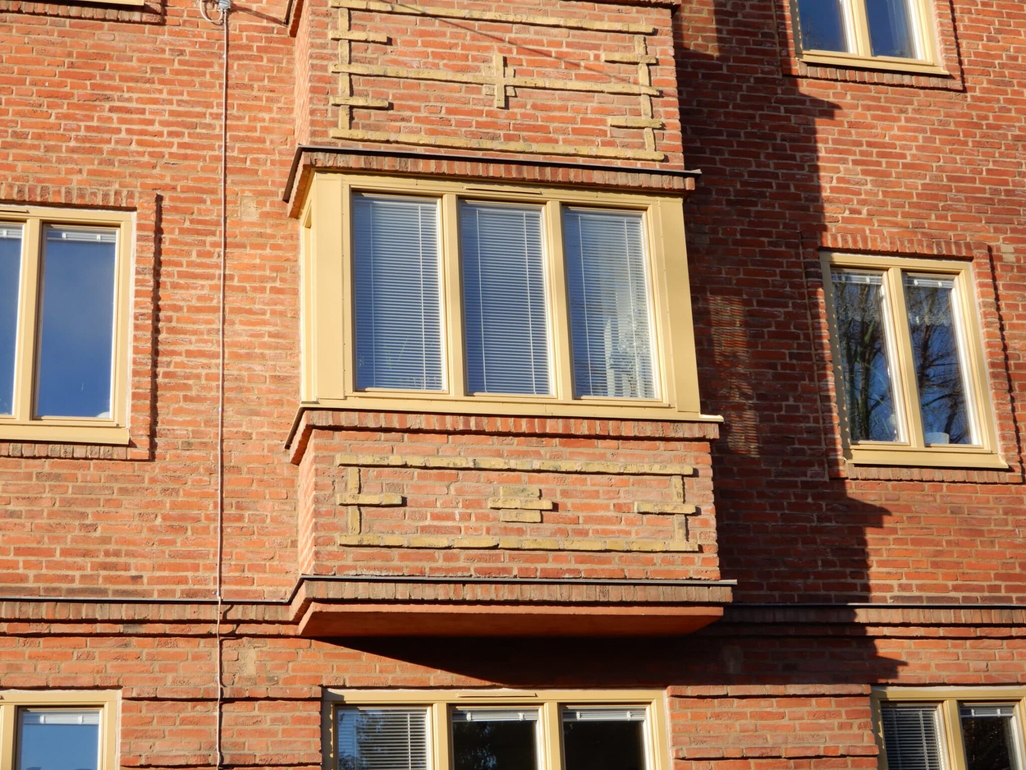 Närbild på nybytta fönster med gulbeige karmar och persienner på röd tegelfasad – fönsterbyte i Malmö utfört av Mockfjärds.