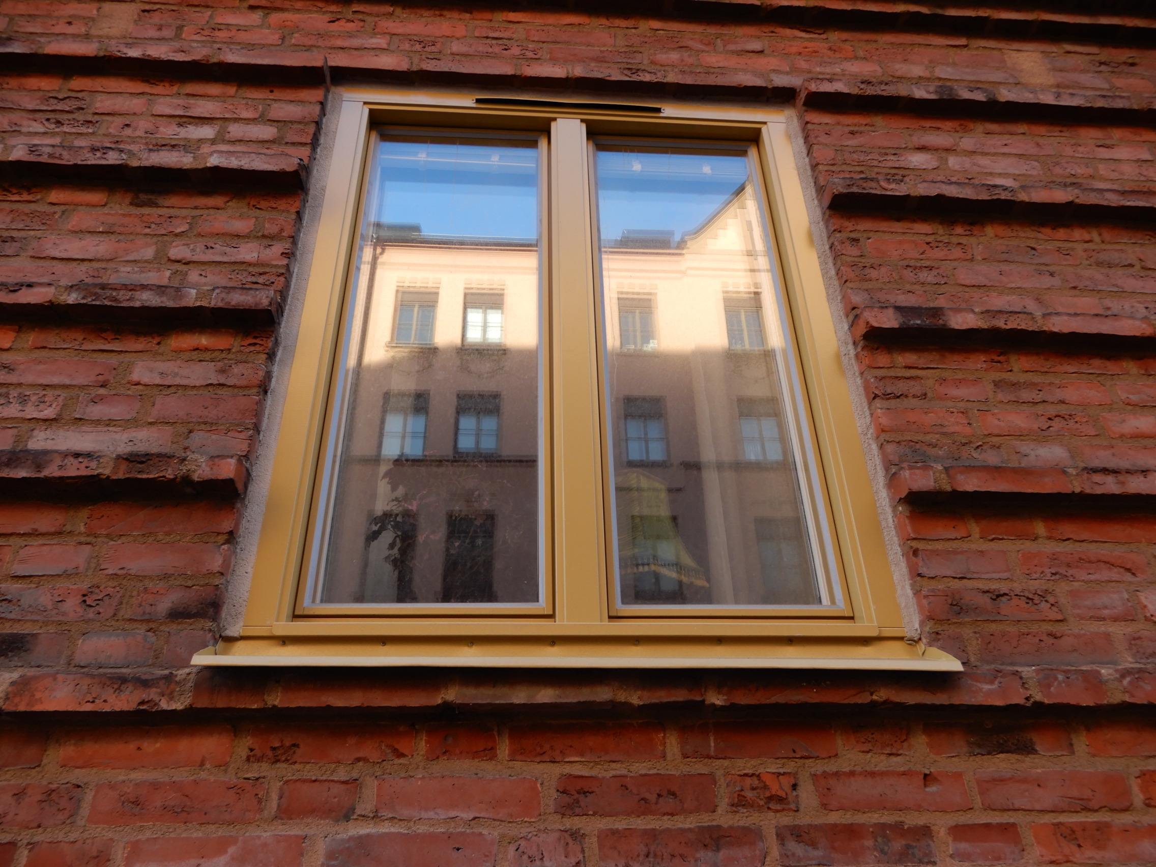 Närbild på nybytt sidohängt fönster med gulbeige karm på röd tegelfasad – fönsterbyte i Malmö utfört av Mockfjärds.