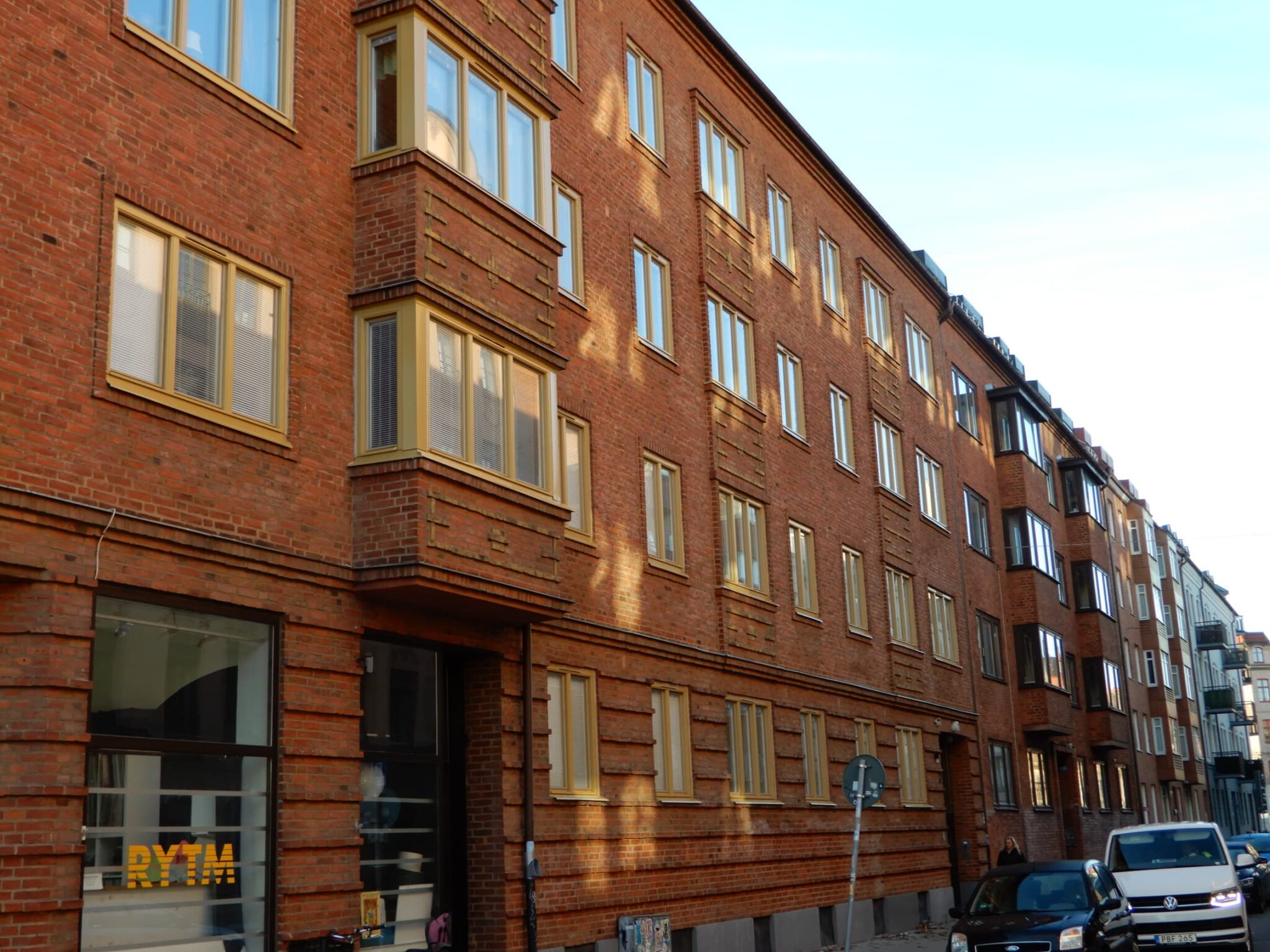 Gatuvy av lång tegelfasad med nybytta fönster med gulbeige karmar i Malmö – byte av 179 fönster utfört av Mockfjärds.