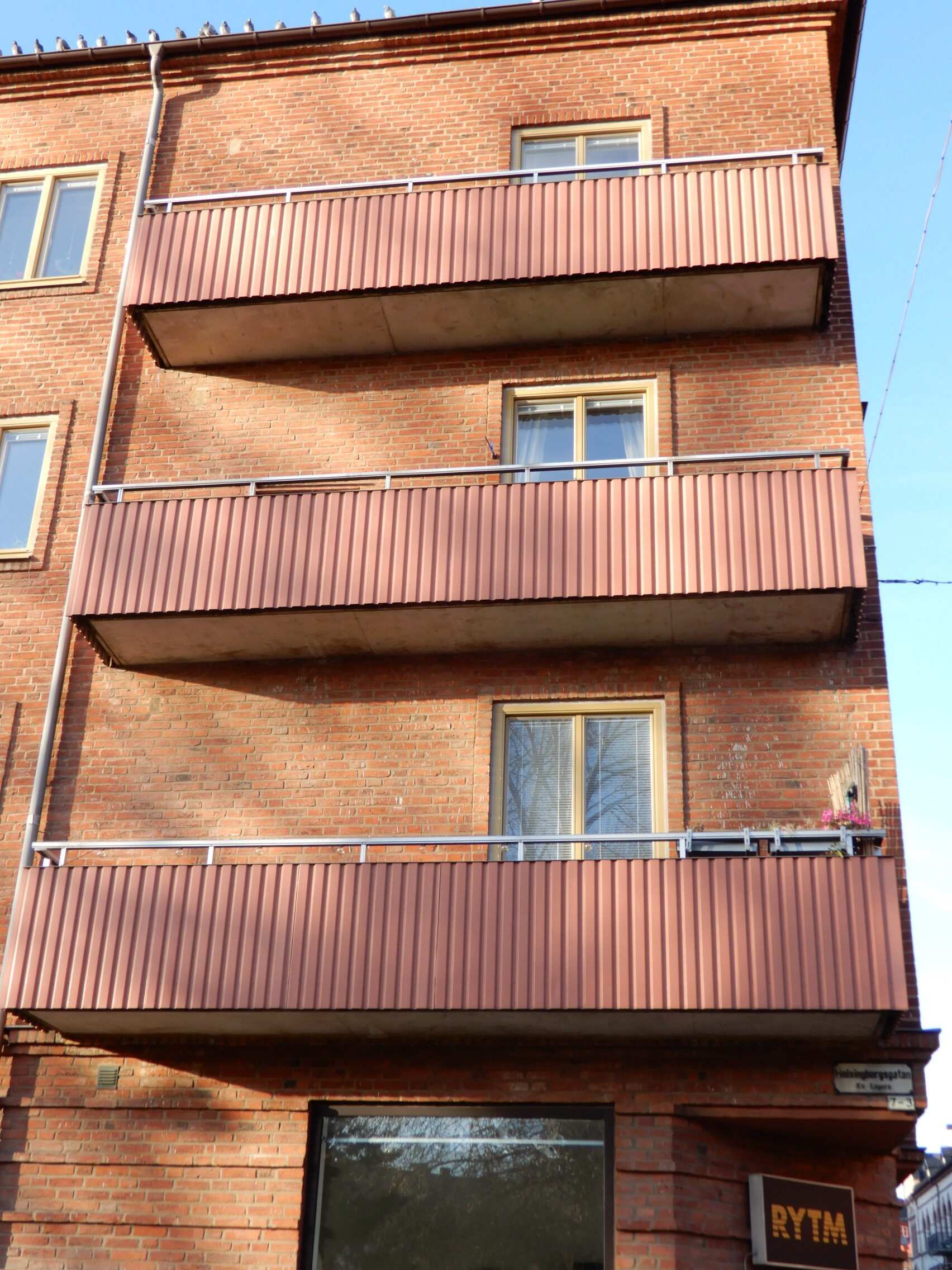 Fasaddetalj med nybytta fönster och röda plåtbalkonger på tegelhus – fönsterbyte i Malmö utfört av Mockfjärds.