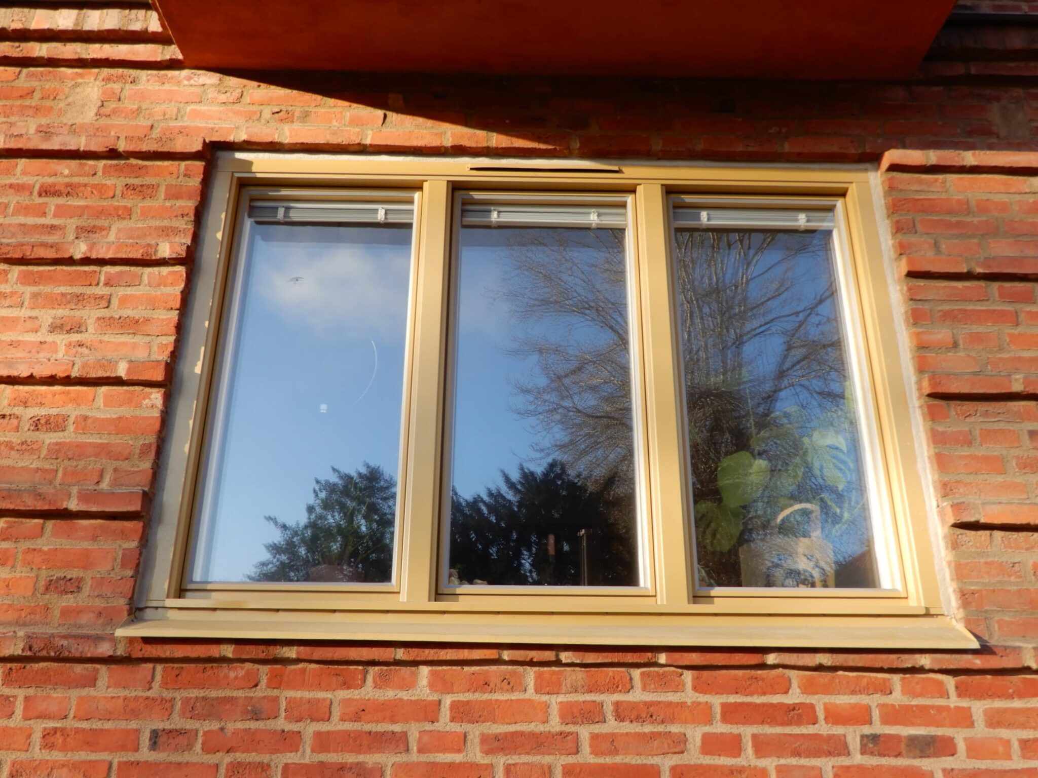 Närbild på nybytt trefönster med gulbeige karm på röd tegelfasad – del av byte av 179 fönster i Malmö utfört av Mockfjärds.