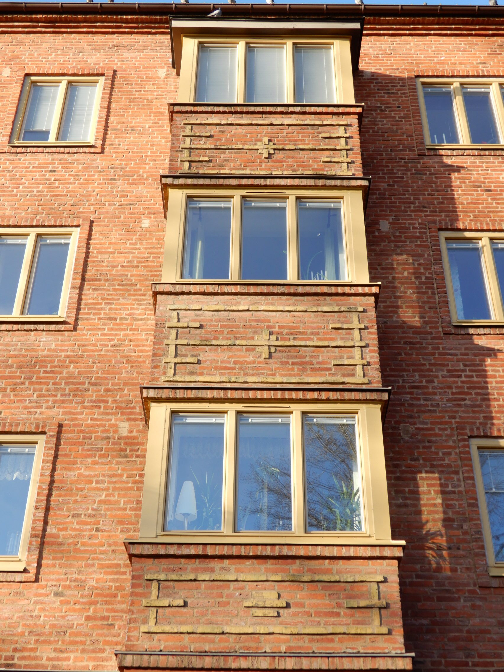 Fasaddetalj med nybytta fönster med gulbeige karmar i vertikalt utskjutande fasadparti – fönsterbyte i Malmö utfört av Mockfjärds.