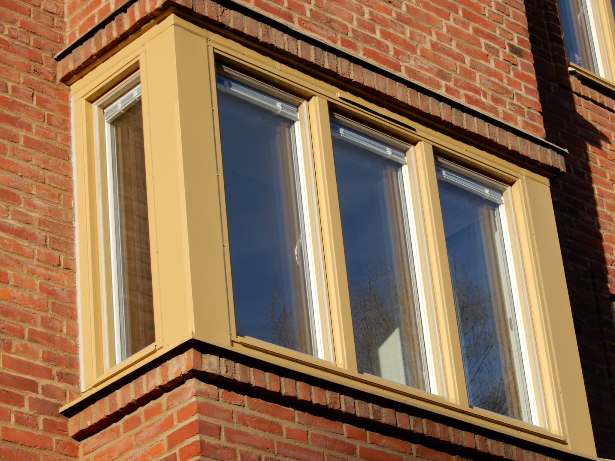 Närbild på nybytt burspråksfönster med gulbeige karm på röd tegelfasad – unikt fönsterbyte i Malmö utfört av Mockfjärds.