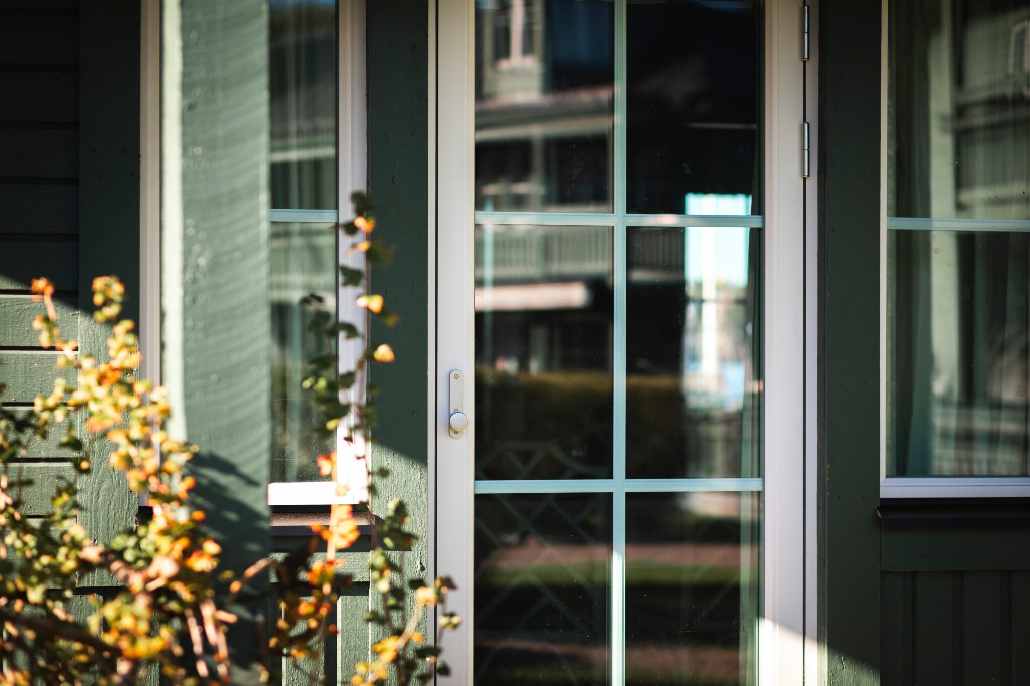 Utåtgående balkongdörr med spröjs och vit karm på grön träfasad – nytt Svanenmärkt fönster i aluminiumbeklätt trä, Fågelbro 7, Värmdö.