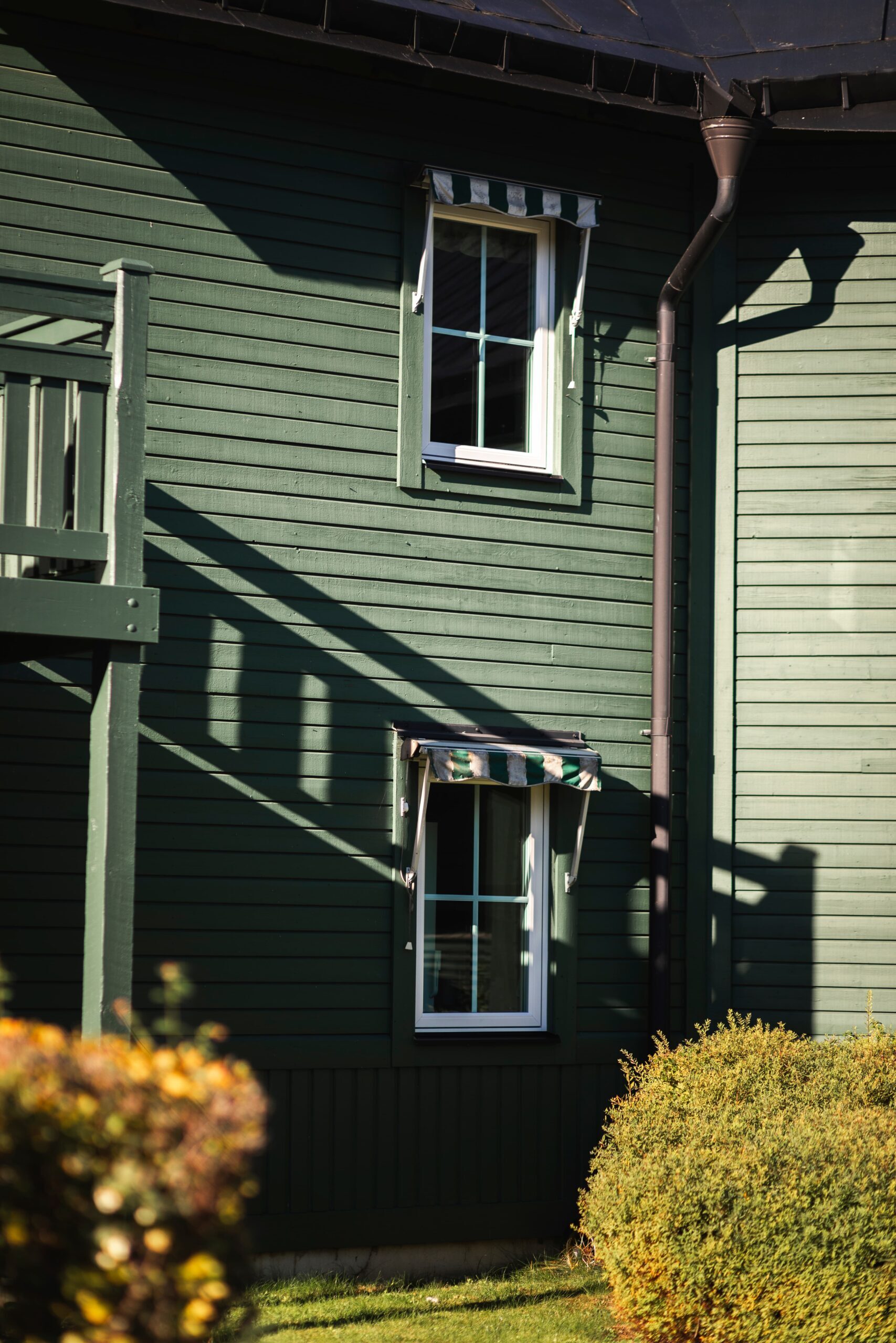 Spröjsade fönster med vita karmar och markiser på grön träfasad – fönsterbyte med Svanenmärkta 3-glasprodukter i Fågelbro 7 på Värmdö.