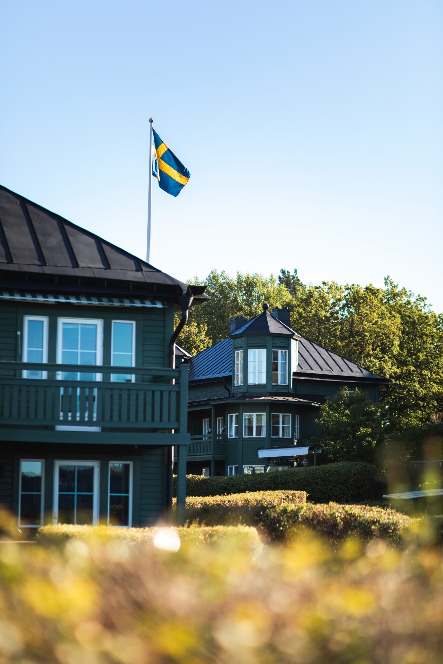 Grönt trähus med nybytta spröjsade fönster och svensk flagga – Fågelbro 7 på Värmdö, sju hus med Svanenmärkta fönster i aluminiumbeklätt trä.