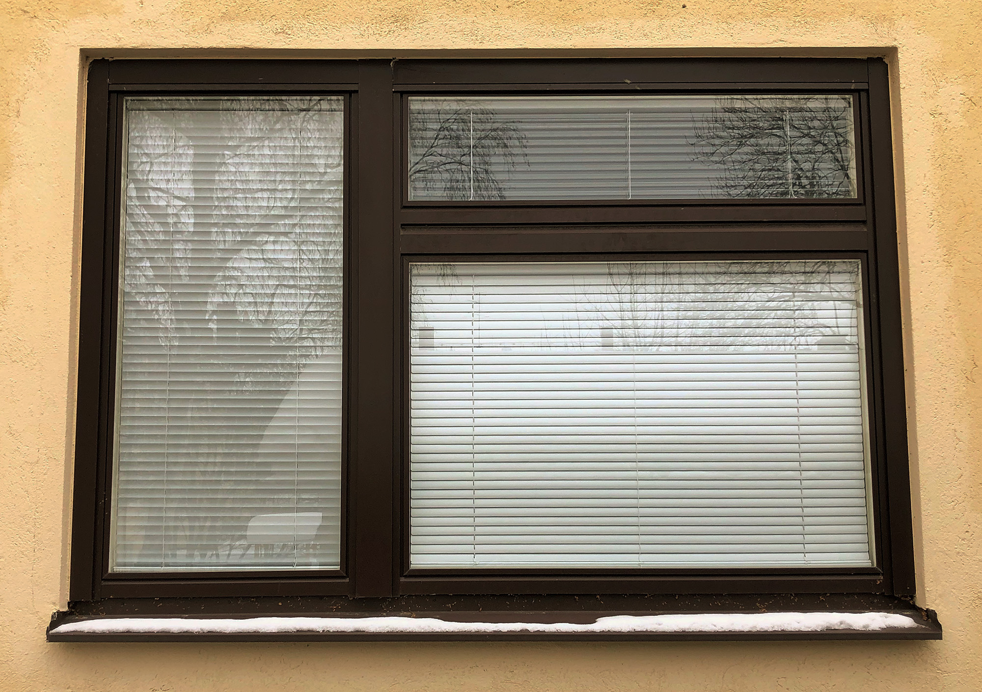 Närbild på nybytt fönster med mörk karm och inbyggda persienner på gul putsfasad – fönsterbyte i centrala Sundbyberg av Mockfjärds.