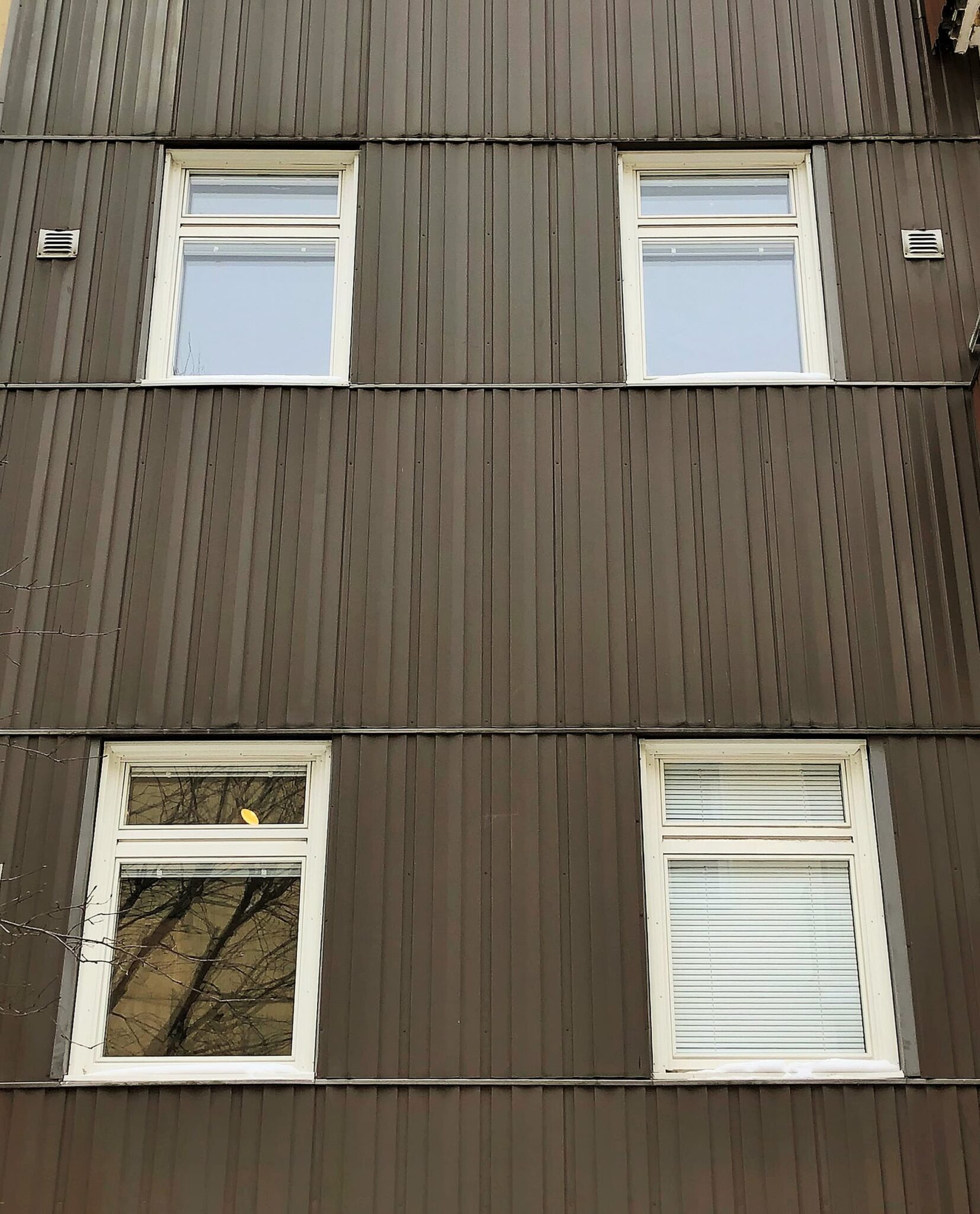 Nybytta fönster med vita karmar på mörk plåtfasad – del av byte av ca 120 fönster i centrala Sundbyberg utfört av Mockfjärds.