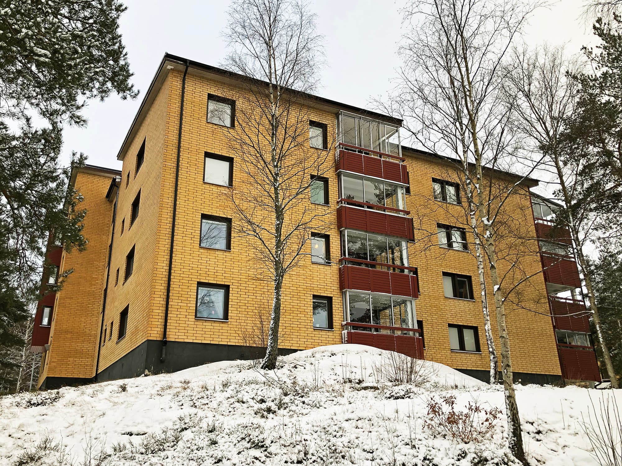 Exteriör av flervåningshus med gul tegelfasad, röda balkonger och inglasade balkonger – del av byte av ca 900 fönster med mörka karmar utfört av Mockfjärds.