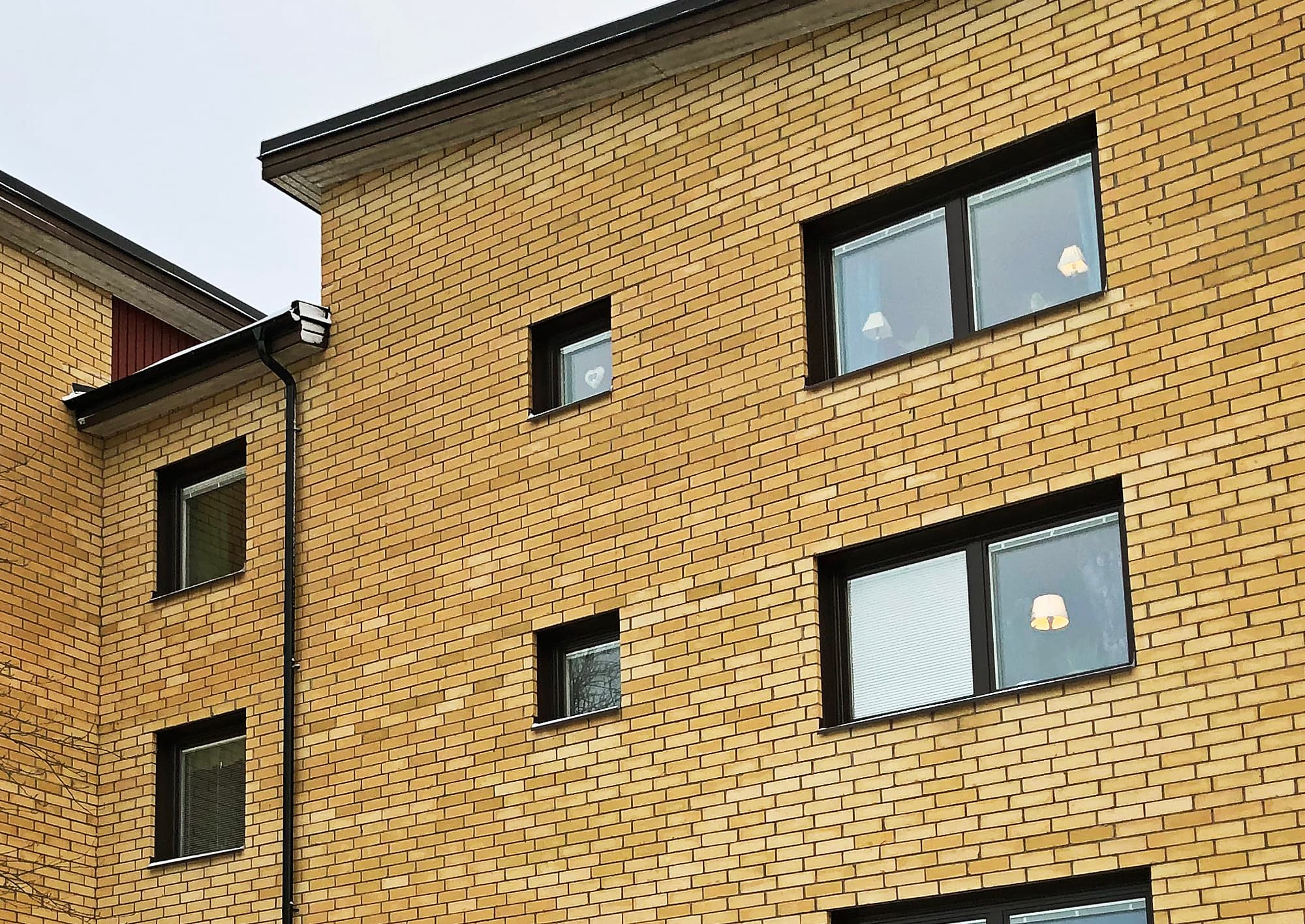 Närbild på nybytta fönster med mörka karmar på gul tegelfasad – storskaligt fönsterbyte av ca 900 fönster i bostadsrättsförening utfört av Mockfjärds.